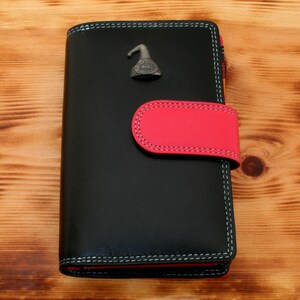 May include: Black leather wallet with a red flap and a silver metal charm. The charm is shaped like a bird with a small bell on its head.