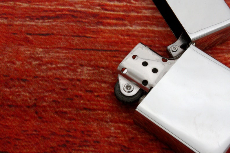 Puede incluir: Un encendedor plateado con una superficie texturizada y una rueda en el lateral. El encendedor est&aacute; abierto y la tapa est&aacute; volteada hacia atr&aacute;s.