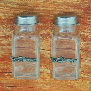 May include: A set of two glass salt and pepper shakers with silver lids and a pewter race car design on the front.