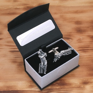 May include: A black gift box with a silver plaque that says "You're a legend!"  The box contains two silver cufflinks featuring a cricket player in action.