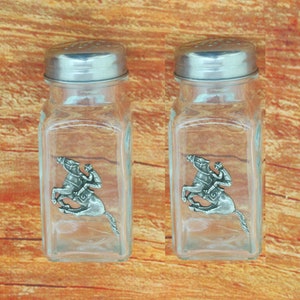 May include: A set of two glass salt and pepper shakers with silver lids. Each shaker features a pewter figurine of a jockey riding a horse.