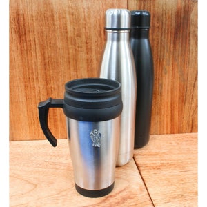 May include: A set of three stainless steel travel mugs. Two are tall and slender, one is shorter and has a handle. The shorter mug has a small angel design on the front.