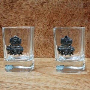 May include: Two clear glass shot glasses with a pewter locomotive design on the front.