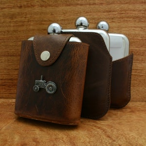May include: Three silver hip flasks with a brown leather carrying case. The case has a metal tractor design on the front.
