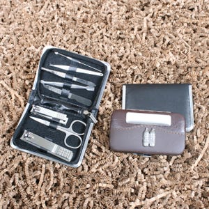 May include: A black zippered manicure kit with various stainless steel tools, including nail clippers and scissors. Next to it are two small cases, one black and one brown, with a decorative silver emblem.