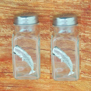 Könnte beinhalten: Zwei Salz- und Pfefferstreuer aus Glas mit silbernen Deckeln. Jeder Streuer enthält eine Zinn-Walfigur im Inneren.