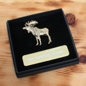 May include: A gold-colored moose figurine in a black velvet box with a gold-colored plaque that reads "Free Engraving Message".