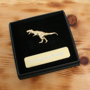 May include: A gold-colored Tyrannosaurus Rex dinosaur figurine in a black velvet box with a gold-colored plaque that reads "Free Engraving Message".