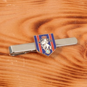 May include: A silver tie clip with a blue, red and white enamel shield featuring a white horse and the text "REME" in white.