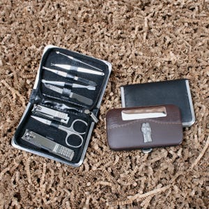 Könnte beinhalten: Ein schwarzes Maniküre-Set mit verschiedenen Edelstahlwerkzeugen, darunter Nagelknipser, Scheren und Feilen. Ein braunes und schwarzes Lederetui mit silbernem Akzent und ein kleines schwarzes Etui sind ebenfalls vorhanden.