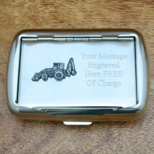 May include: A silver metal cigarette case with a small tractor design on the front. The case has a hinged lid and a message that says "Your Message Engraved Here FREE Of Charge".