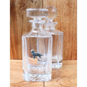 Può includere: Due caraffe di vetro trasparente con tappi. Una caraffa contiene una statuetta di un cane in peltro.