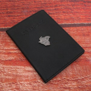 May include: Black leather passport holder with a silver embossed outline of Spain and the word "Spain" written in cursive.