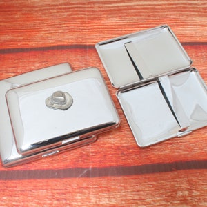 May include: Two silver cigarette cases, one with a small silver cowboy hat charm. The cases are open and empty.
