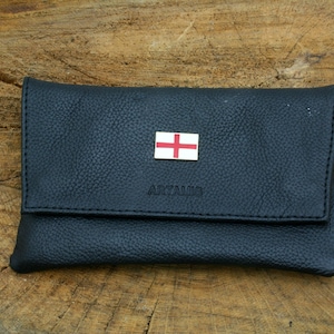 May include: A black leather tobacco pouch with a small red and white cross flag and the word "ARTAMIS" embossed on the front.