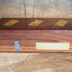 May include: A wooden box with a brass plaque that says "Your Message Engraved Here For Free". The box has three inlaid dominoes with gold-colored dots. A small metal figure of a person wearing a hat is attached to the box.