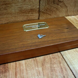 May include: A wooden box with a brass plaque that says "Your Message Engraved Here For Free". The box is closed and has a small metal figure on top.