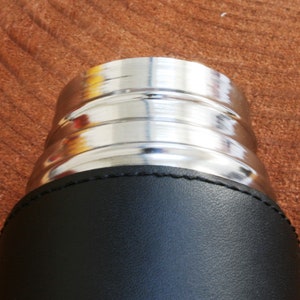 K&ouml;nnte beinhalten: Nahaufnahme der Oberseite einer schwarzen, lederbezogenen Thermoskanne mit einem silbernen Metalldeckel.