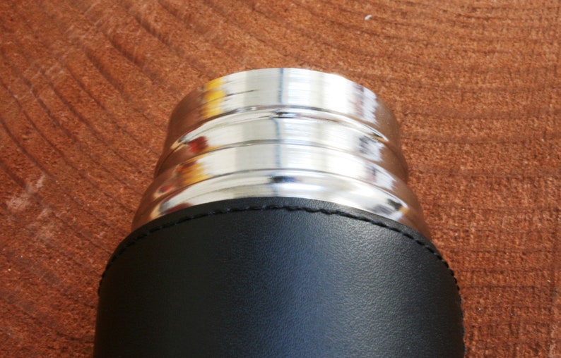 K&ouml;nnte beinhalten: Nahaufnahme der Oberseite einer schwarzen, lederbezogenen Thermoskanne mit einem silbernen Metalldeckel.
