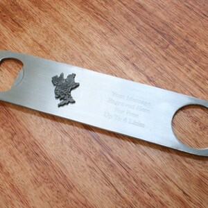 May include: A silver bottle opener with a small engraved design. The opener has a large opening for bottle caps and a smaller opening for twisting off bottle caps. The text "Your Message Engraved Here For Free Up to 364 Lines" is engraved on the opener.
