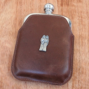 May include: A brown leather hip flask with a silver top and a silver design of two figures holding hands.