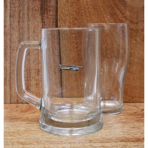 Könnte beinhalten: Ein klares Glasbierkrug mit Henkel und einem kleinen silbernen Hubschrauber-Anhänger an der Seite.