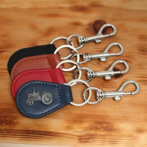 May include: Leather keychains in black, brown, red, and navy blue, each with a silver-tone metal clasp and keyring. The navy blue keychain features a tractor emblem.