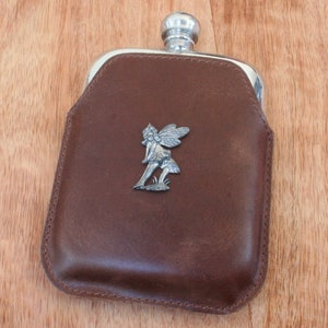 May include: A brown leather flask with a silver metal top and a silver metal fairy figurine attached to the front.
