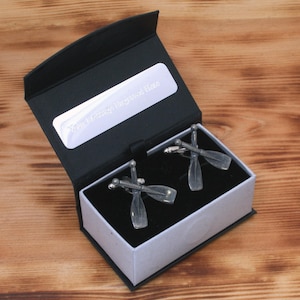 May include: A black gift box with a white interior, containing two silver cufflinks shaped like crossed oars. The box has a white label with the text "You Can Always Row Back Home".