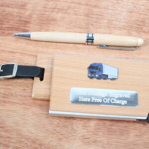 May include: Wooden luggage tag with a blue truck design and a silver plate that says "Your Message Engraved Here Free Of Charge". The tag has a black leather strap with a silver buckle.