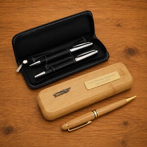 May include: A black zippered pen case containing two black pens with silver accents, a rectangular bamboo wooden pen case with a gold-colored plaque reading Your Message Engraved Here For Free, and a bamboo wooden pen with gold-colored trim.
