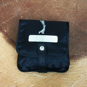 Op de afbeelding: Een zwarte ritszak met een zilveren golfspelerfiguur en een zilveren plaquette met de tekst "Geloof altijd dat je kunt".