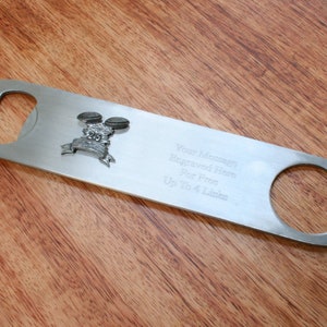 May include: Silver bottle opener with a small engraved design of two drumsticks and a drum. The opener has a space for a personalized message, "Your Message Engraved Here For Free Up to 4 Lines".