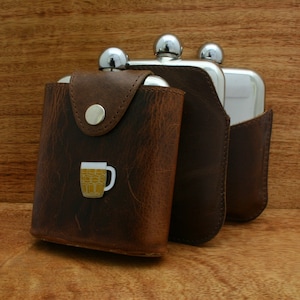 May include: Three brown leather hip flasks with silver tops. The flask on the left has a small beer mug design on the front.