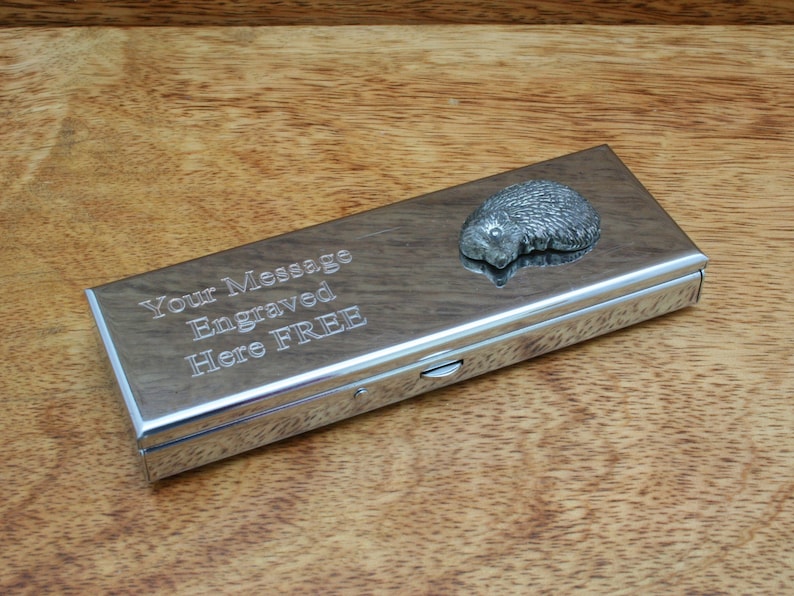 May include: A silver metal box with a hedgehog design on the lid. The box has a hinged lid and a sliding latch. The box is engraved with the text "Your Message Engraved Here FREE".