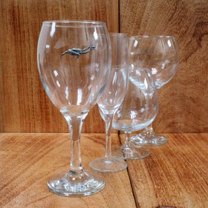 May include: Four clear glass wine glasses on a wooden surface. One glass has a small silver figurine of a diver inside.