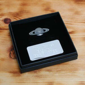 May include: A silver-colored Saturn planet pin in a black velvet box with a silver plaque that reads "To my amazing son, you are a star, love from Dad".