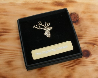 May include: A gold stag head pin in a black velvet box with a gold plaque that reads "In Loving Memory".