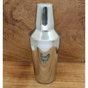 Op de afbeelding: Een zilveren cocktailshaker met een voskopontwerp aan de voorkant.
