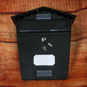 May include: Black metal mailbox with a slot for mail, a keyhole, and a blank nameplate. The mailbox has a decorative scalloped top.