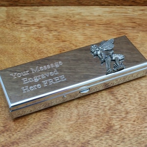 Puede incluir: Una caja de metal plateada con un diseño de hada en la tapa. La caja tiene una tapa con bisagras y un pestillo deslizante. La caja está grabada con el texto "Your Message Engraved Here FREE".