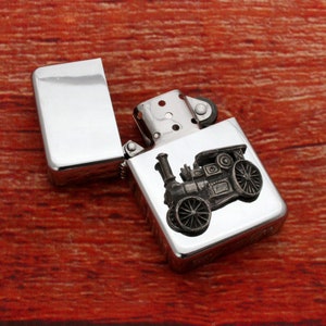May include: A silver lighter with a detailed engraving of a vintage steam engine. The lighter is open, showing the flint and wick.