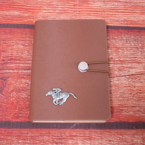 May include: A brown leather notebook with a silver horse and rider design and a silver button closure.
