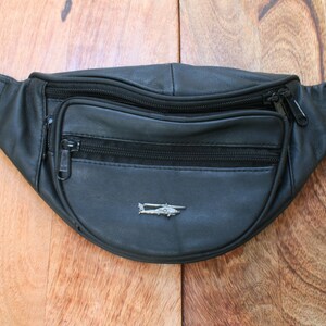 Könnte beinhalten: Schwarze Leder-Bauchtasche mit einem Reißverschlussfach und einer silbernen Helikopter-Anstecknadel.