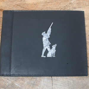 May include: Black leather journal with a silver embossed design of a hunter with a gun and a dog.