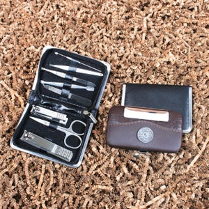 Puede incluir: Un kit de manicura negro con cremallera con herramientas de acero inoxidable, que incluyen cortaúñas, tijeras y limas. También hay un estuche de cuero marrón con un acento plateado y un tarjetero negro.