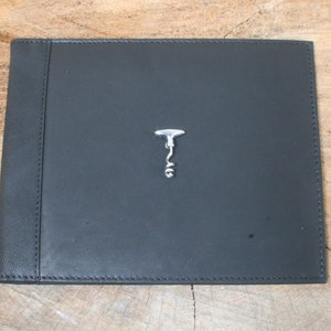 May include: A black leather-bound journal with a silver corkscrew emblem on the front cover.