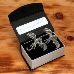 May include: A black gift box containing a silver dragon cufflink set. The box has a white interior and a silver plaque with the text "Your Message Engraved Here".