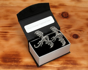 Puede incluir: Una caja de regalo negra con un juego de gemelos de dragón de plata en su interior. La caja tiene un interior blanco y una placa plateada con el texto "Su mensaje grabado aquí".