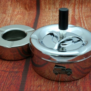May include: A chrome ashtray with a rotating lid and a small truck design on the bottom. The ashtray has a separate, smaller, round ashtray that can be used for cigarette butts.